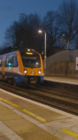 Toma-De-Video-Vertical-Temprano-En-La-Mañana-Del-Tren-De-Cercanías-Que-Llega-A-La-Plataforma-De-La-Estación-De-Tren-En-Bushey,-Reino-Unido